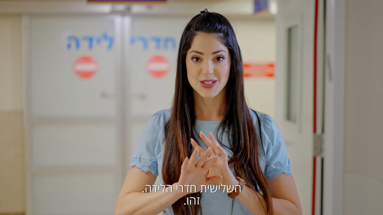 קדר מתוך סרט תדמית: אישה עומדת במסדרון בית חולים ליד דלתות "חדרי לידה"